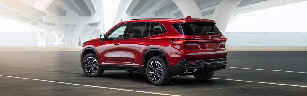 A red Buick Enclave SUV parked under a bridge with a scenic backdrop.